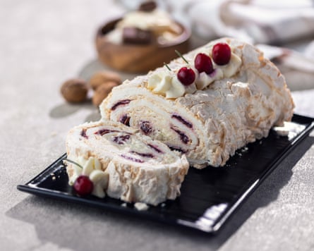 Sliced cream roll with berries on a black plate, dusted with powdered sugar.