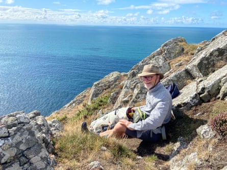 A smiling man sits on a rocky coast high up over the sea