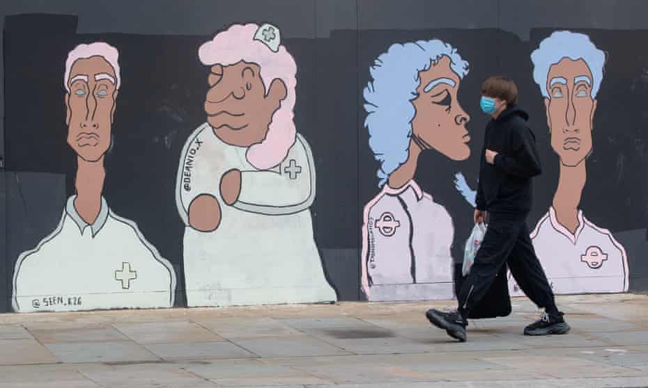 A man wearing a protective face mask passes a mural showing BAME medical and transport workers, in Waterloo, London.