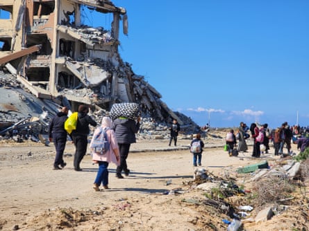 People carry possessions as they walk past ruined and flattened buildings