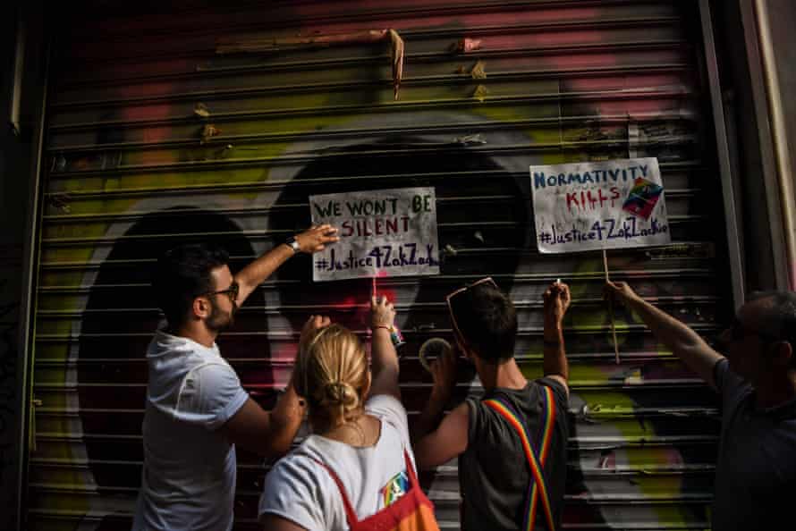People paste posters reading ‘We won’t be silent’ on the shutters of the shop where Zak Kostopoulos was killed.