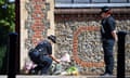 A female police officer lays flowers by a wall, as another looks on