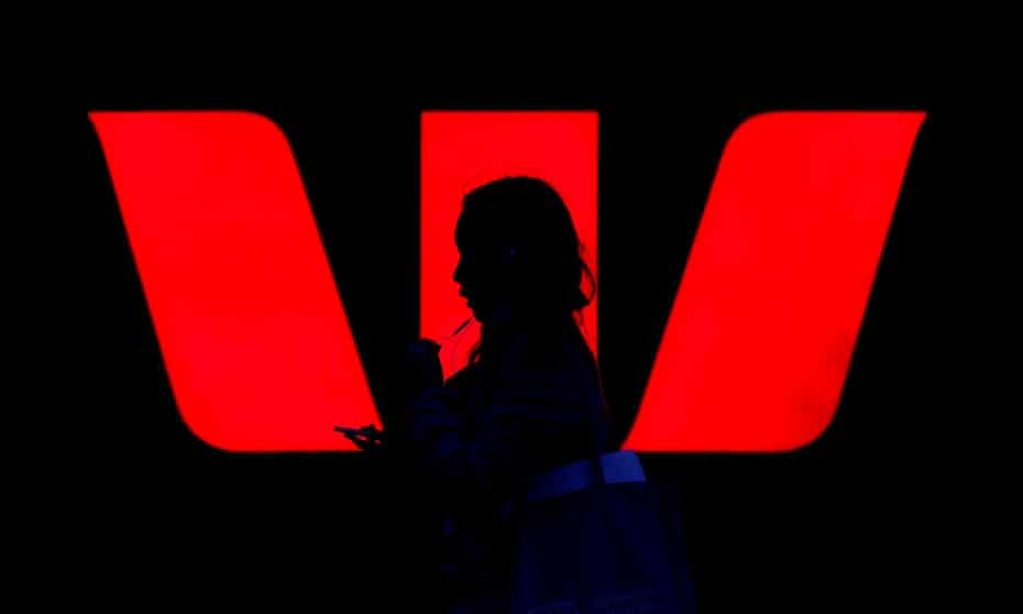 A woman walks past an illuminated logo for Westpac