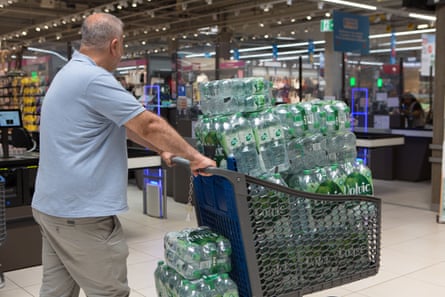 A man in a supermarket, trolley heaped with bottles of water.