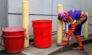 A clown ties his shoelace at the kerbside