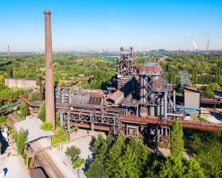 The rusty remains of factory including its chimney amid a sea of trees
