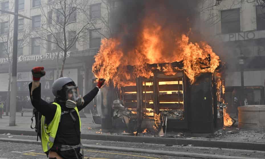 A protestor celebrates in front of a burning kiosk in the Champs-Élysées, Paris.