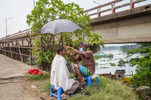 A barber at the roadside shaves a worker beneath a parasol