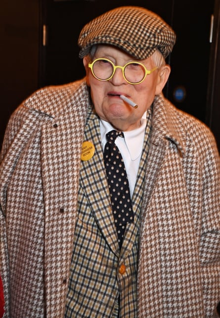 Hockney wears a tweed suit, jacket and flat cap in 2023.