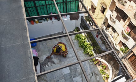 An aerial shot shows a woman crouching to wash the tiles of a balcony with a cloth
