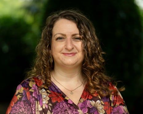 Elizabeth Arif-Fear with curly brown hair wearing a colorful floral top smiles outdoors against a blurred green background