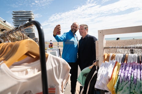 Starmer posing for a selfie with a man on the seafront with racks of clothing around them