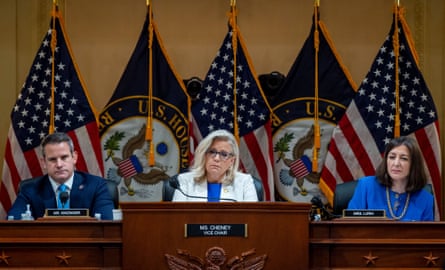 a man and two women sit at table with flags behind them
