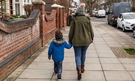 A mother and son walking on the pavement holding hands shot from behind