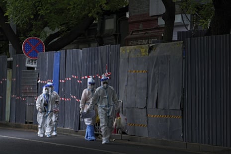 Workers in protective clothing walk by retail shops and neighbourhood surrounded by metal barricades for Covid-19 control in Beijing on 26 June 2022.