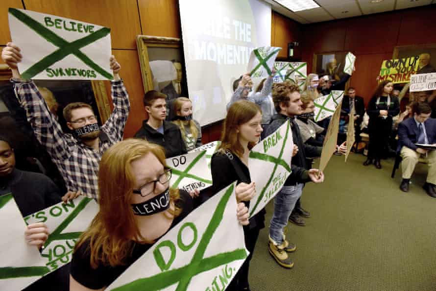 Supporters of victims of sexual abuse by Larry Nassar, hold up signs during a Michigan State Board of Trustees meeting, in December 2017.