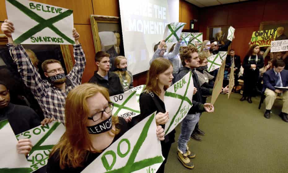 Supporters of victims of sexual abuse by Larry Nassar hold up signs during a Michigan State Board of Trustees meeting on Friday.