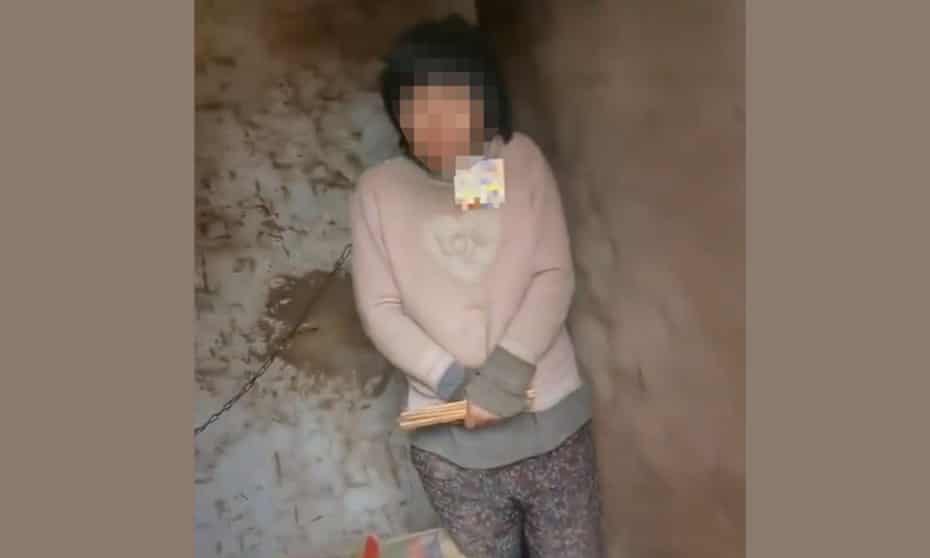 A screenshot of the video showing a woman in China with a chain around her neck in a shack.
