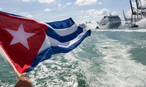 A man waves a Cuban flag as cruise ship Adonia sails out of Miami’s port escorted by tugboats.