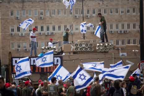 Protesters hold flags as they are standing on a model of a tank during a demonstration calling for equality in military service near the official prime minister’s office in Jerusalem on 26 March.