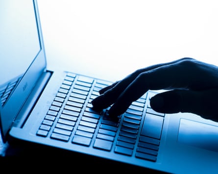 a hand in silhouette taps a laptop keyboard