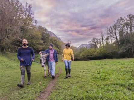 Three people walking a donkey in a green meadow in Asturias, Spain