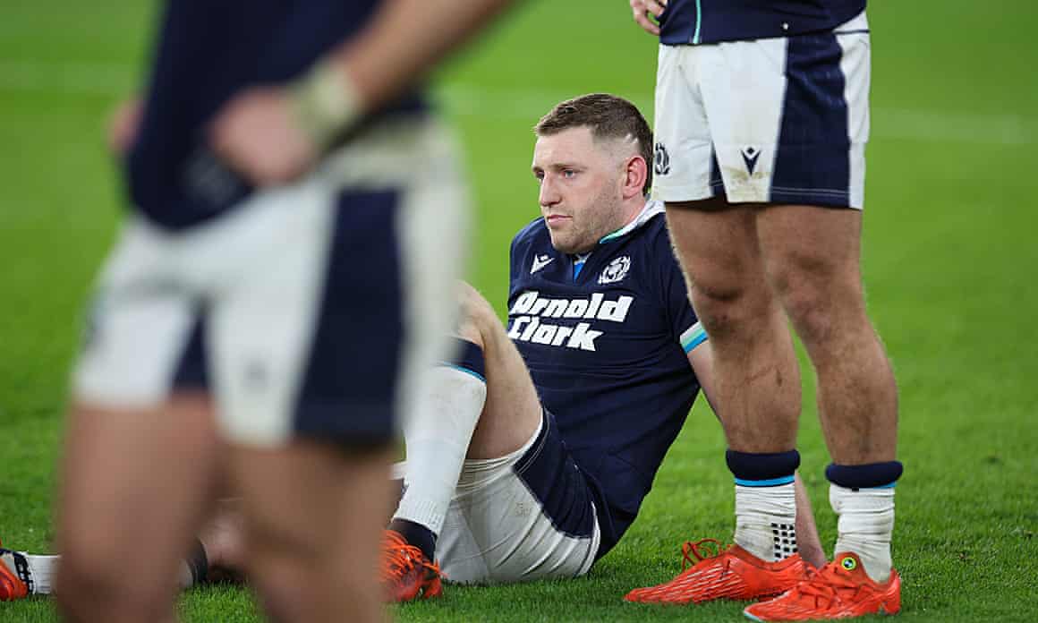 Finn Russell sits on the pitch at Twickenham looking dejected.