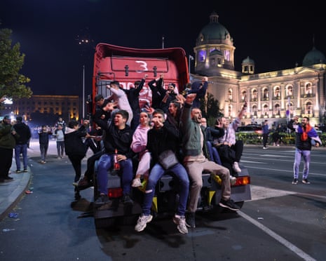 Young adults raise their fists on the back of an articulated lorry cab on a city street