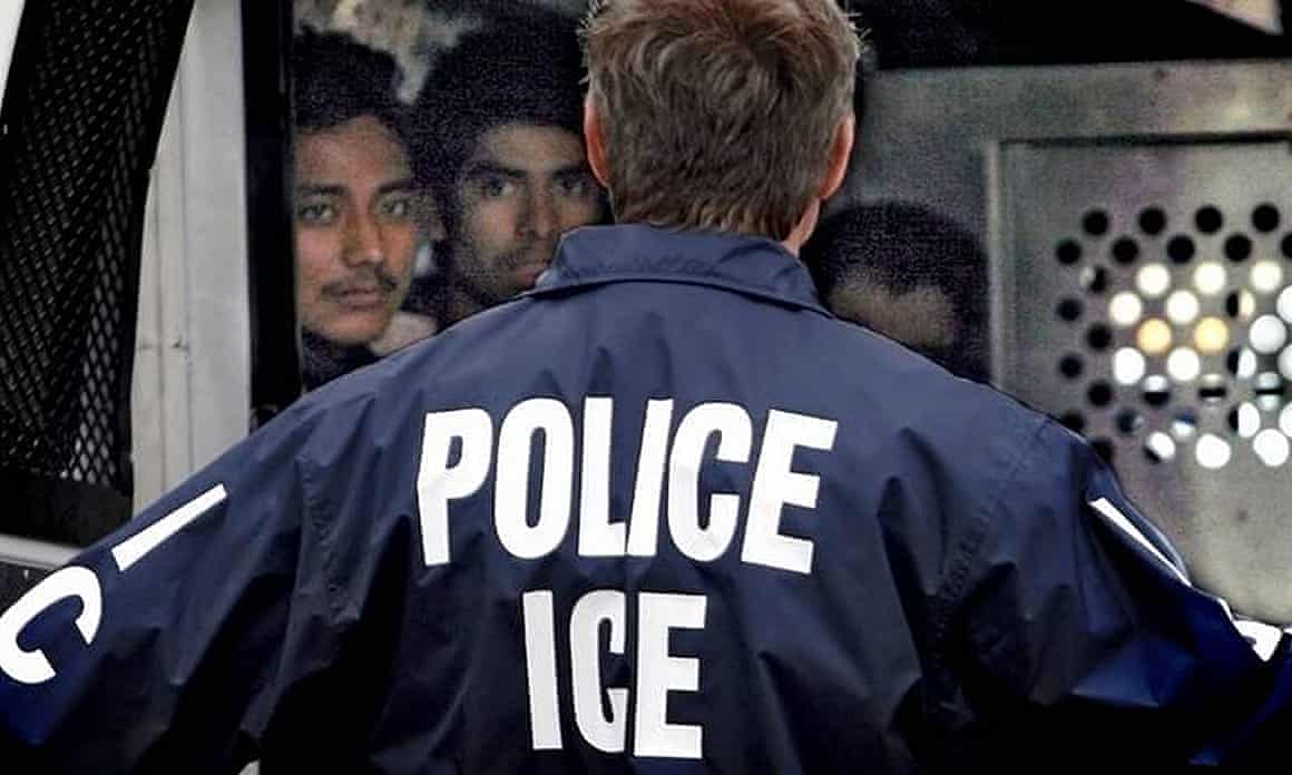 An officer with Immigration and Customs Enforcement talks to people detained in a van