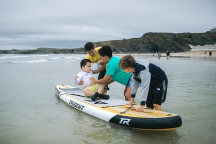Tom Butler sits disabled student, Brody Walters, on a surfboard, while his mum, Kelly, and brother, Chace, steady it against the waves