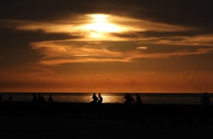 Silhouettes of people in front of the water during sunset