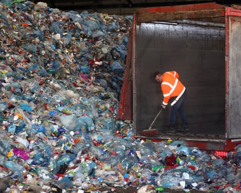 A man clearing a container surrounded by plastic recycling