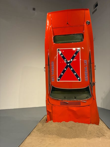 An all-red (or orange?) care with a Confederate flag pained on the roof, on its nose in a pile of sand as if it crashed there.