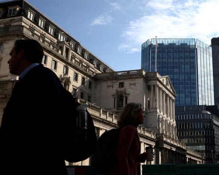People are silhouetted in bright sunshine as they walk outside the Bank of England building.