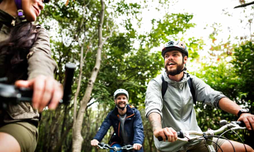 Three people on bikes smile and chat in a forest