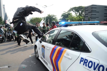 A leaping man kicks the window of a police car