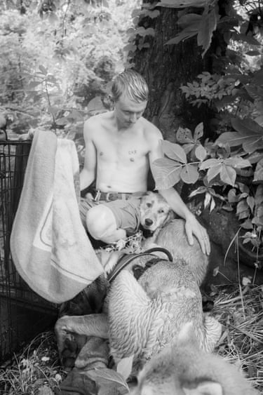 A young man sitting with his dogs on the river bank after a swim