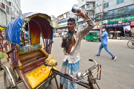 رجل يصب الماء على رأسه وهو يقف في الشارع بجوار عربة ريكشا