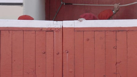 An image of a red wooden cabin with a white strip at the top and a hand coming over the top and a person’s red cap