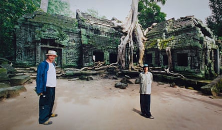 Two people stand within a ruined building with a large tree at Angkor Wat in Cambodia.