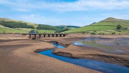 A reservoir reduced to a small channel of water with a bridge and hills in the background