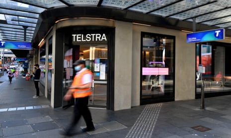 A man in a high-vis jacket wearing a mask walks past a Telstra retail branch in Sydney