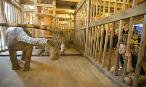 Ein Besucher schaut in einen Käfig mit einem Modelldinosaurier auf der Arche.