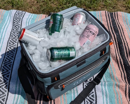 soda cans on ice inside blue cooler, sitting on blanket in grass