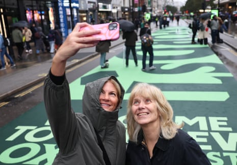 People take selfies as they walk along the traffic-free Oxford Street in London today