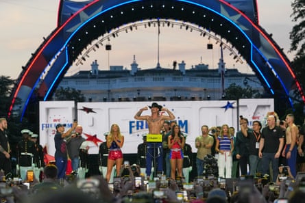 shirtless man stands on stage with arms flexed during weigh-in
