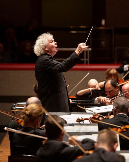 Sir Simon Rattle conducts, baton raised,