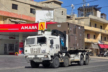 A white, eight-wheeled armoured truck with UN symbols on its doors moves along a street in Tyre in front of a petrol station and low-rise apartment blocks.