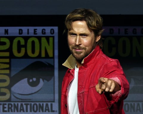 Ryan Gosling in a red jacket points at the camera at a Comic-Con panel