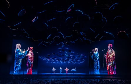 Holograms of the band appear around the stage under blue lighting.